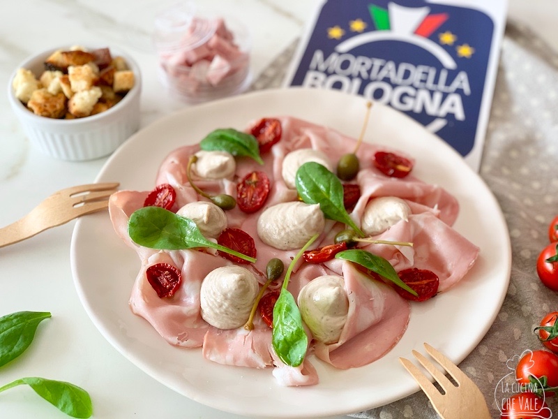 La Mortadella Bologna IGP tonnata è un piatto creativo davvero gustoso dove questo salume viene usata al posto del vitello. E' arricchito con pomodorini confit, salsa tonnata senza uova, spinaci freschi e fiori del cappero.